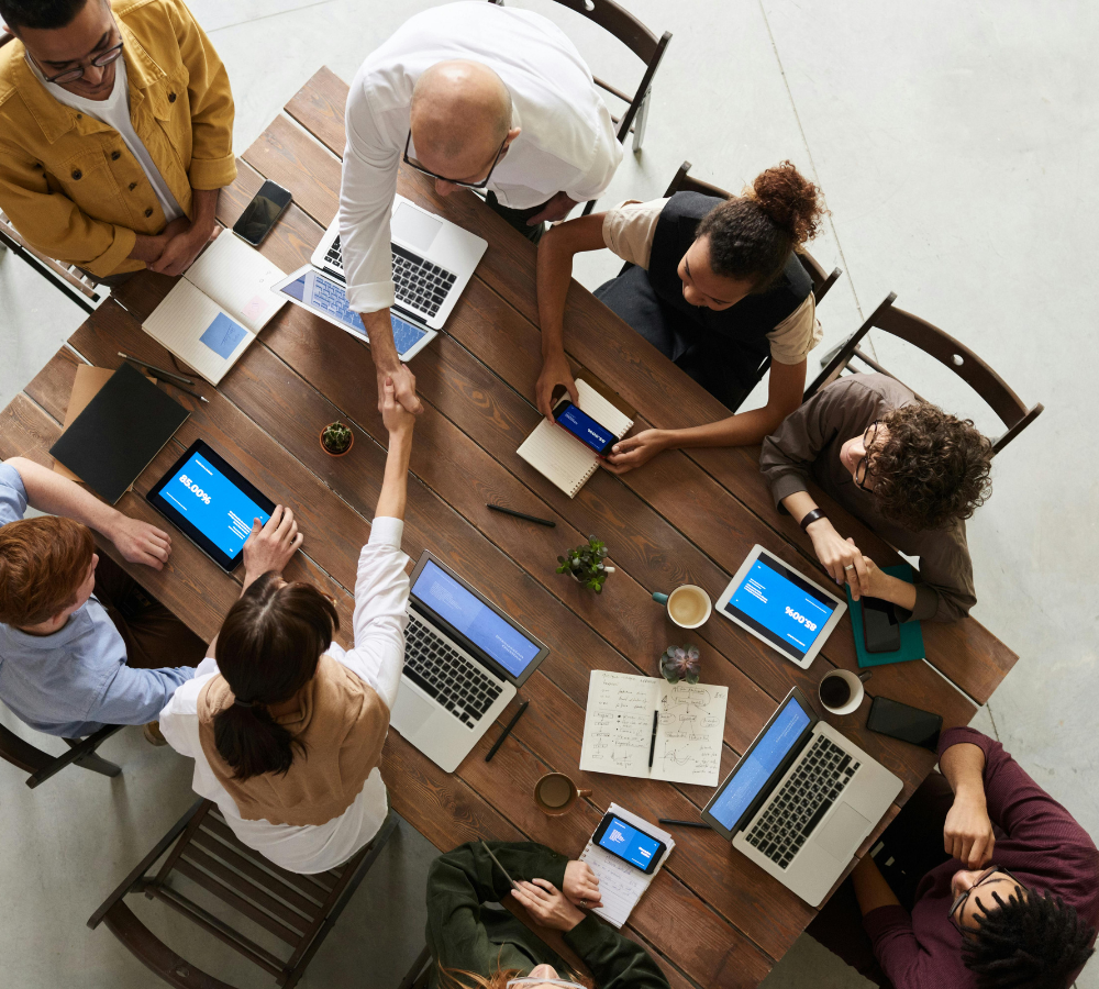 Overhead view of a diverse team collaborating around a table with laptops and tablets.